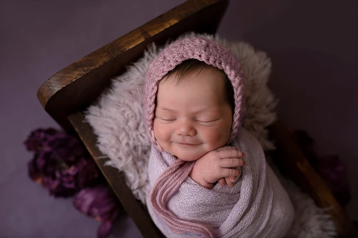 portrait of a smiling baby on a purple background in a fur lined crib with flowers, taken in the studio of Alyssa Renee Photography in Jacksonville, Florida
