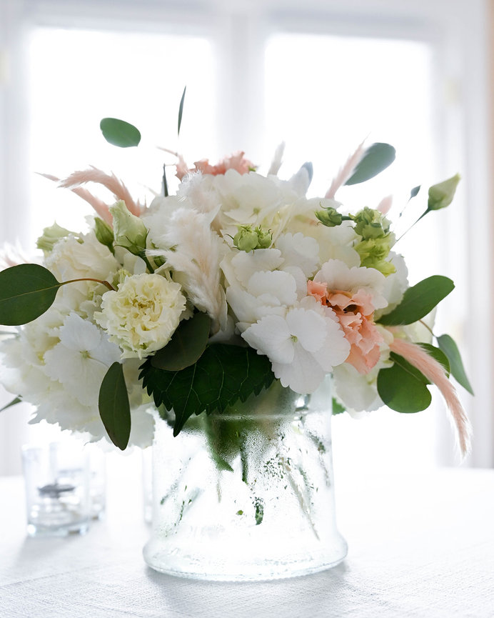 A beautiful bouquet of white and peach flowers in a textured glass vase, set against a bright background.