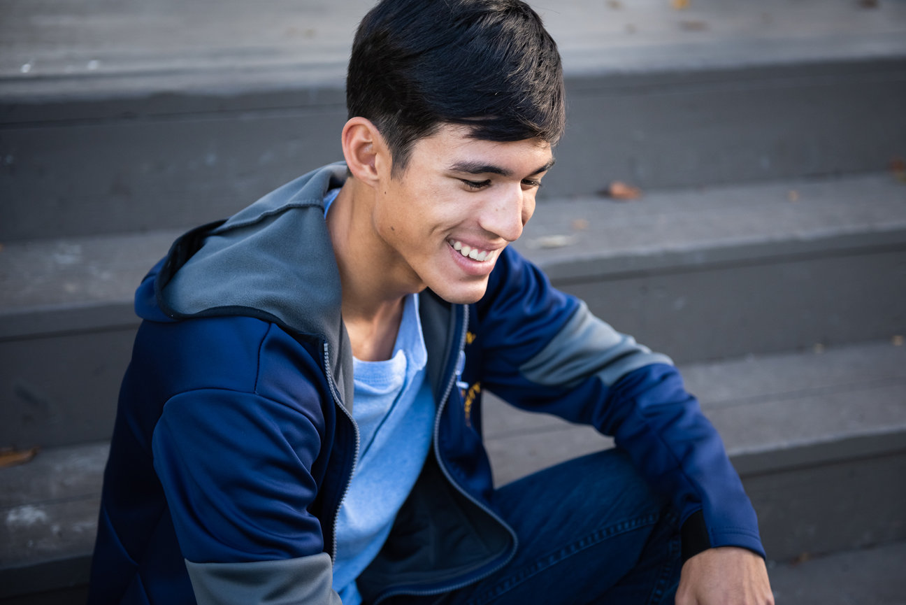 high school senior boy sits on staircase smiling down at ground for graduation photo