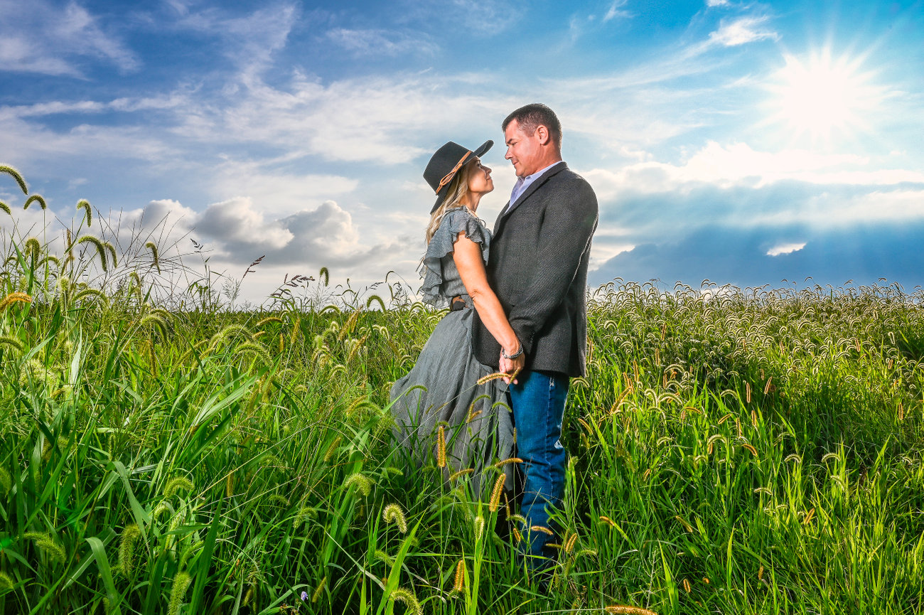 Couple holding hands in a grassy field, under a bright sky with sun rays.