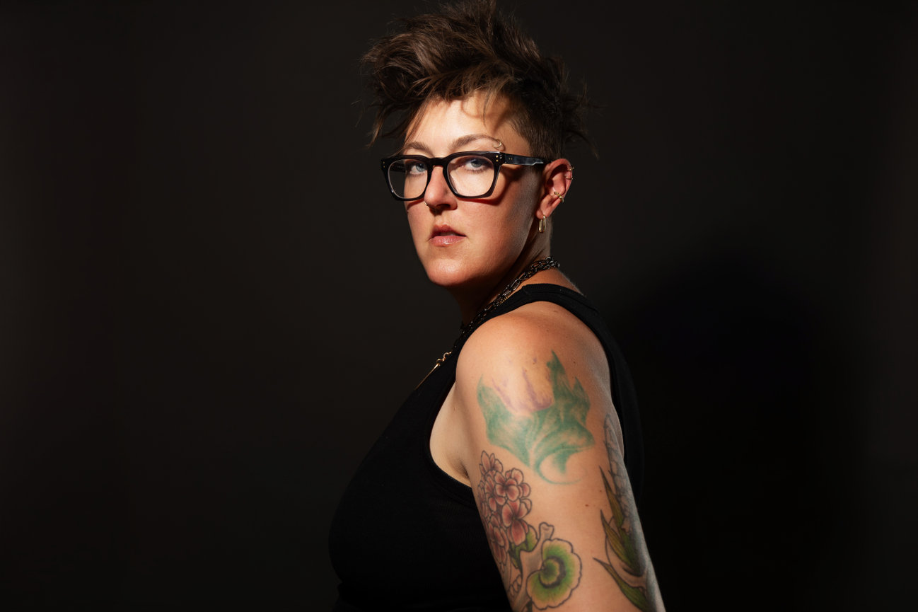 Iowa photographer Jaimy Ellis posed boldly in front of a black background confidently looking at camera.