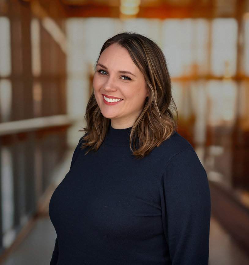 Smiling woman in a dark top, standing in a warmly lit room with blurred background.
