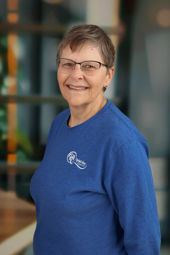 Person smiling, wearing glasses and a blue shirt with a logo, with a blurred background.