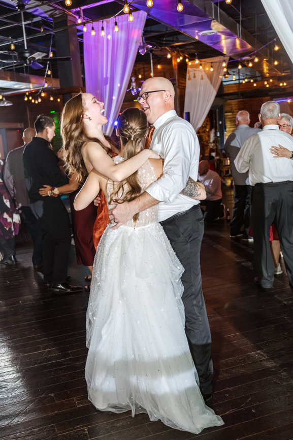 Bride dancing and laughing with guests at a lively wedding reception under string lights.
