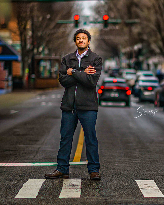 Senior boy with crossed arms standing in middle of urban downtown street with traffic light bokeh — fine art editorial environmental senior portrait by Master Photographer Ty Swartz, Swartz Portraits Houston Texas