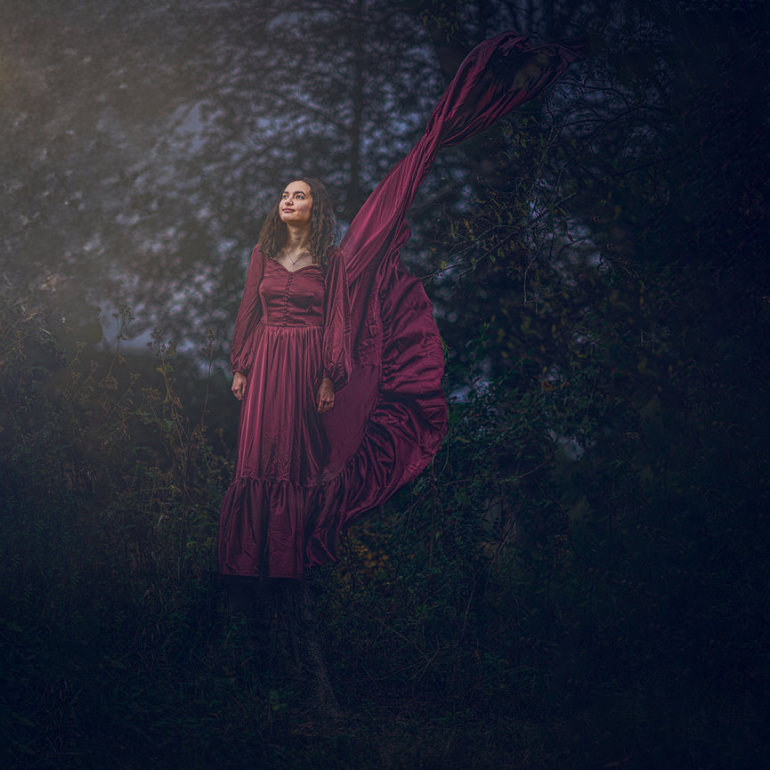 Senior portrait of girl in flowing red velvet dress amid moody Texas forest at dusk, cinematic editorial fine art by Master Photographer Ty Swartz, Swartz Portraits Spring Texas serving The Woodlands and Conroe