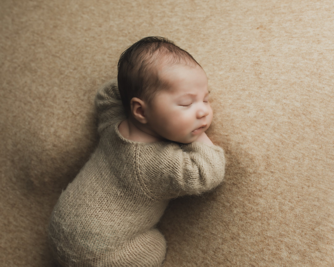 Baby sleeping on a beige surface facing sideways