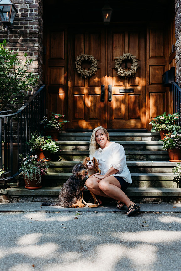 A blond woman with two small dogs sits on steps in front of wooden double doors