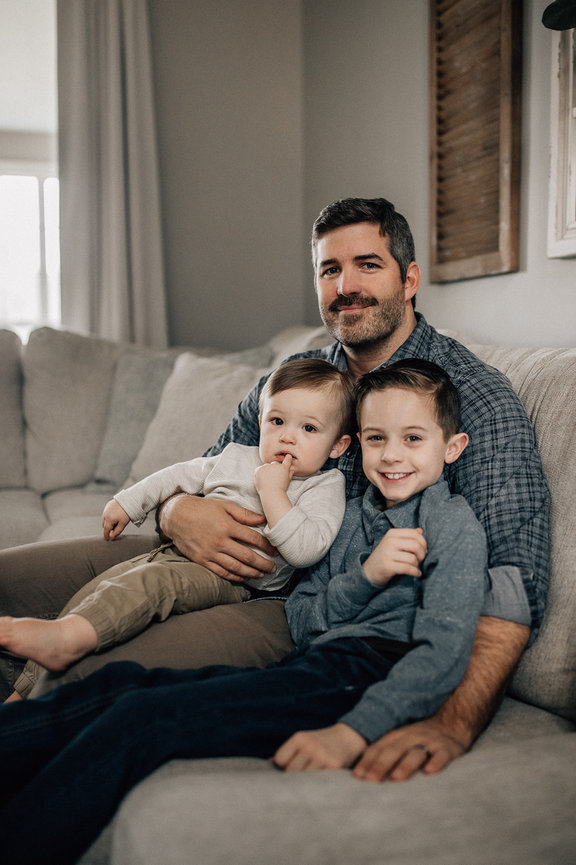 A father sits on a couch with his two young sons during a huntsville Alabama family photoshoot.