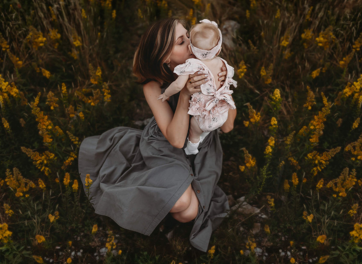 A mother kissing her baby while sitting in a field of flowers during their New Jersey Family Photography Session.