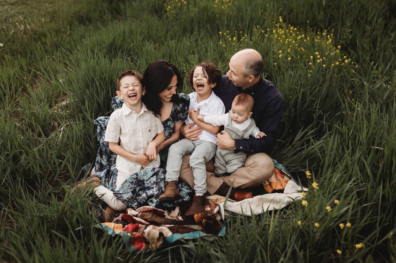A family sitting together in a field and laughing at the Central Park of Morris County.