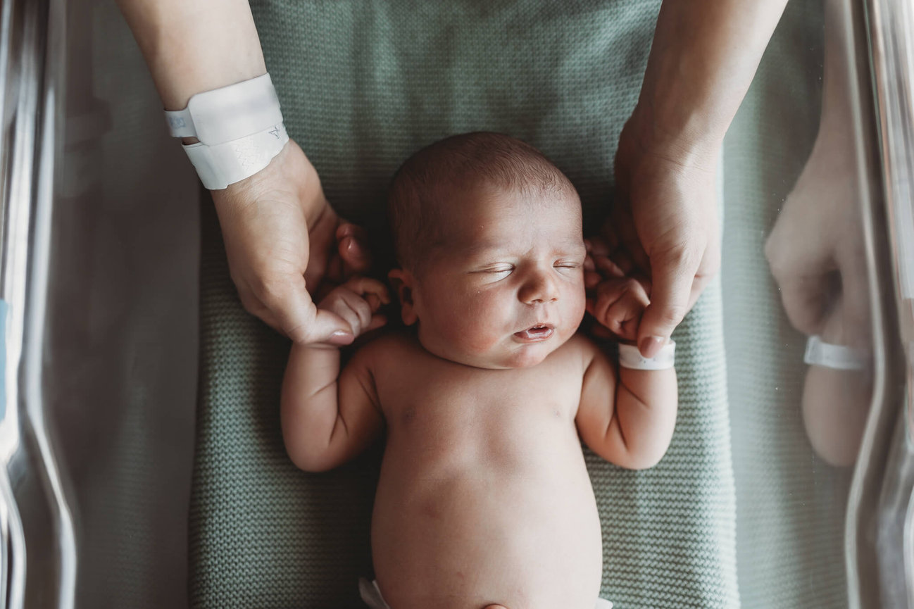 A mother holding her newborns hands in a hospital bassinet during a Monmouth County Medical Center Fresh 48 Session.