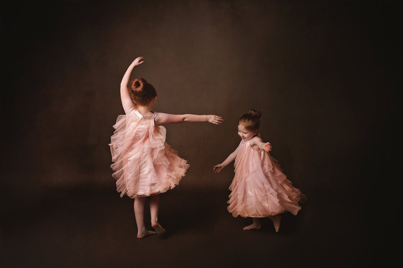 Red haired sisters in pink tulle dresses dance with each other