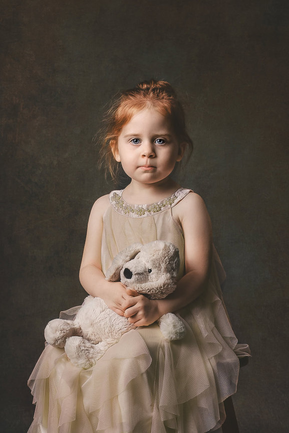 a serious young girl with red hair looks directly into the camera while holding a stuffed dog lovey