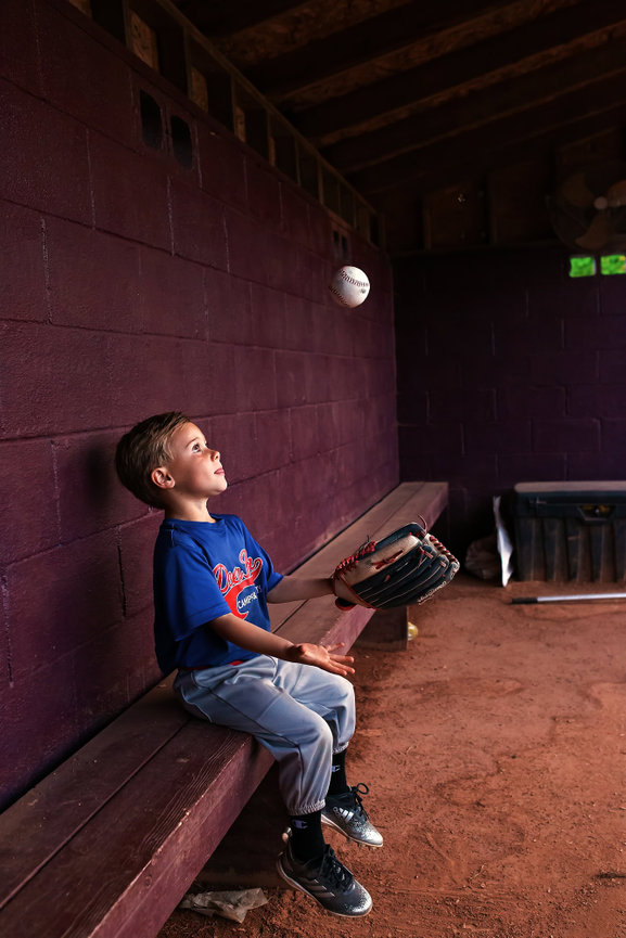 A young baseball player tossed a ball in the dugout
