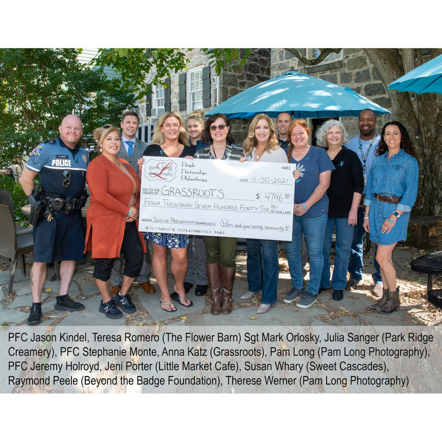 Group of people standing outdoors holding a large check, with a tent and trees in the background