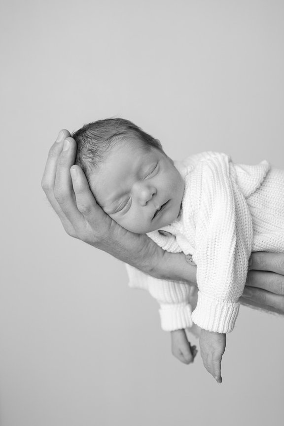 Newborn baby on the side held by his father's hand in black and white