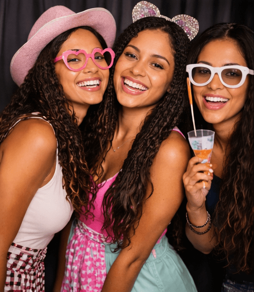 Three women smiling with drinks and glasses at a party