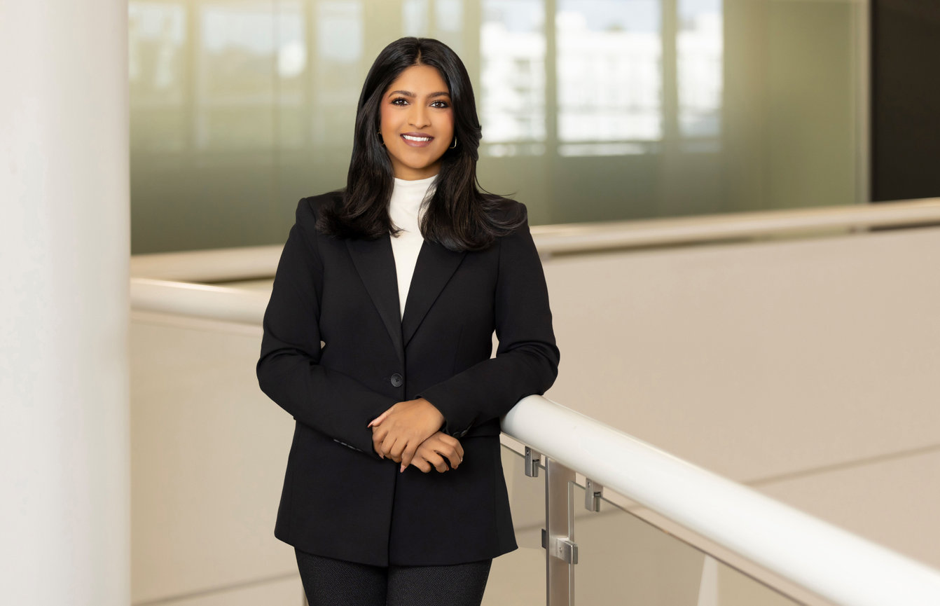 Professional woman in a dark suit standing in a modern office hallway.