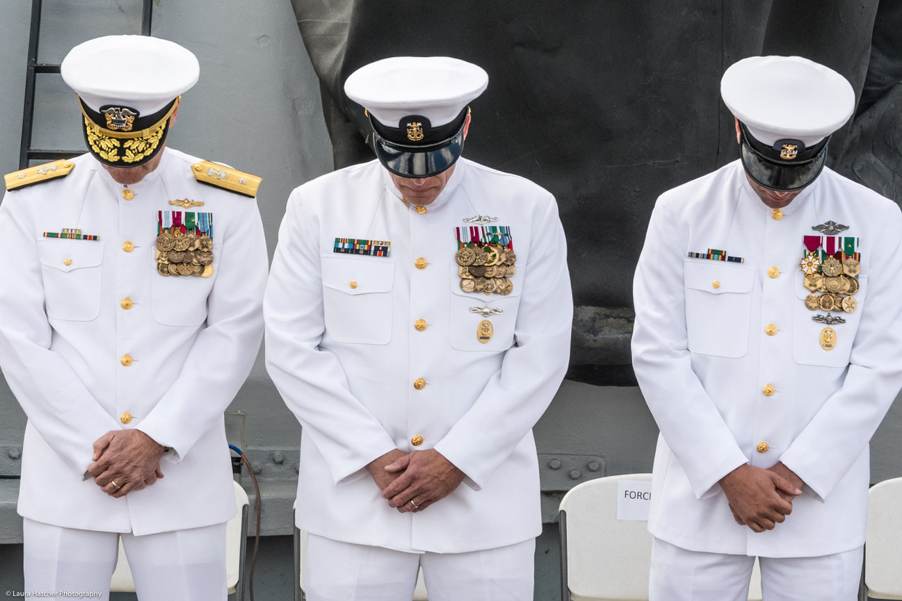 Navy Master Chief bowing with his official party during prayer at his retirement ceremony