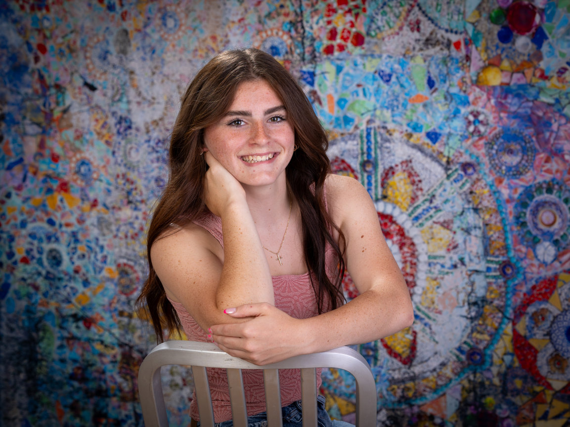 Smiling teen girl leaning on a chair in front of a colorful painted mural.