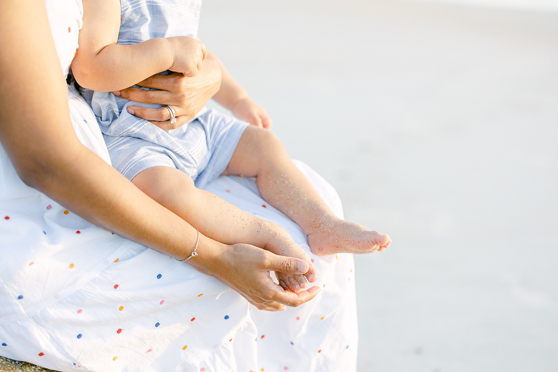 close up of woman holding baby's feet on sandy beach