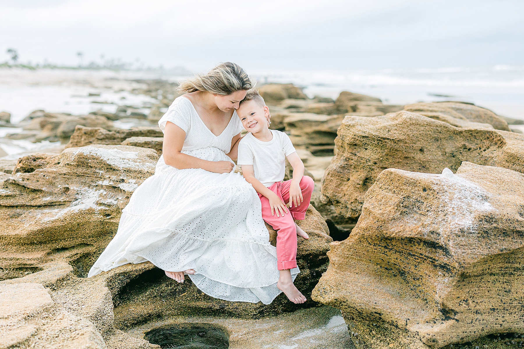 woman in white dress sitting on rocks on beach with little boy