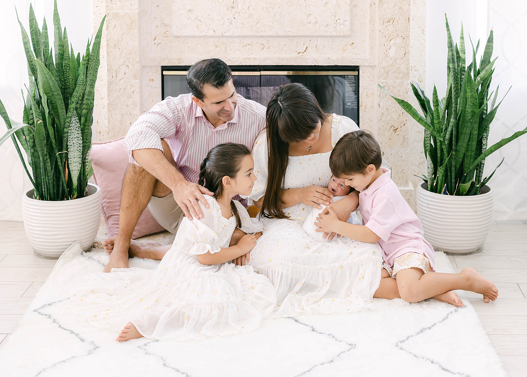 family sitting on carpet holding newborn baby wearing light colors