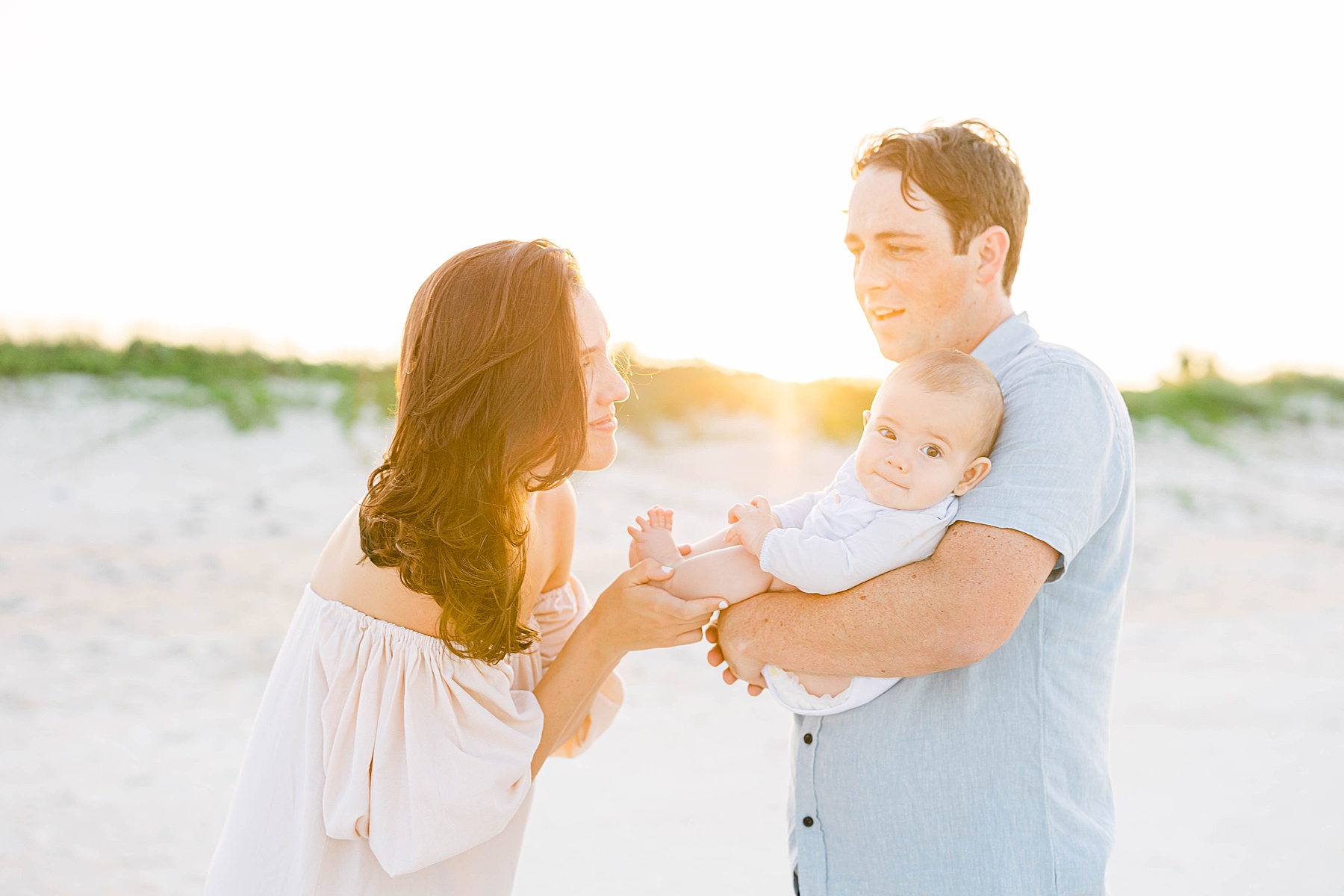 woman and man holding baby at sunset on beach