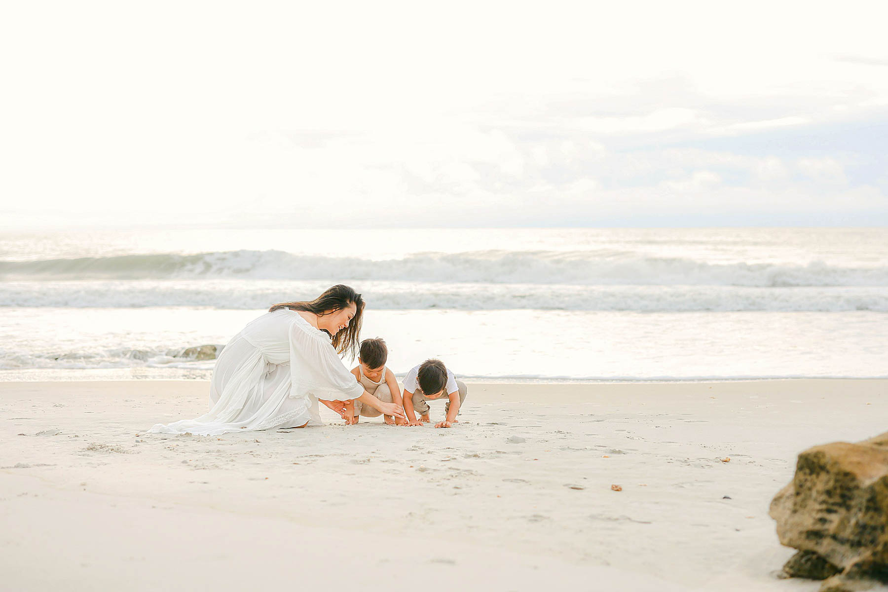woman playing in the sand with boys wearing neutral colors