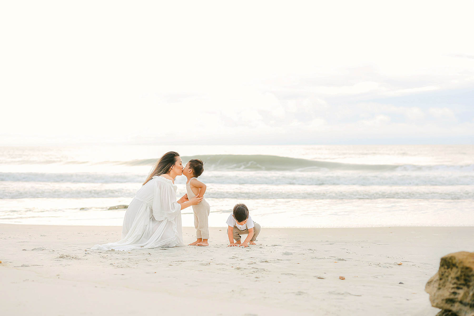 woman wearing white dress playing in the sand with boys