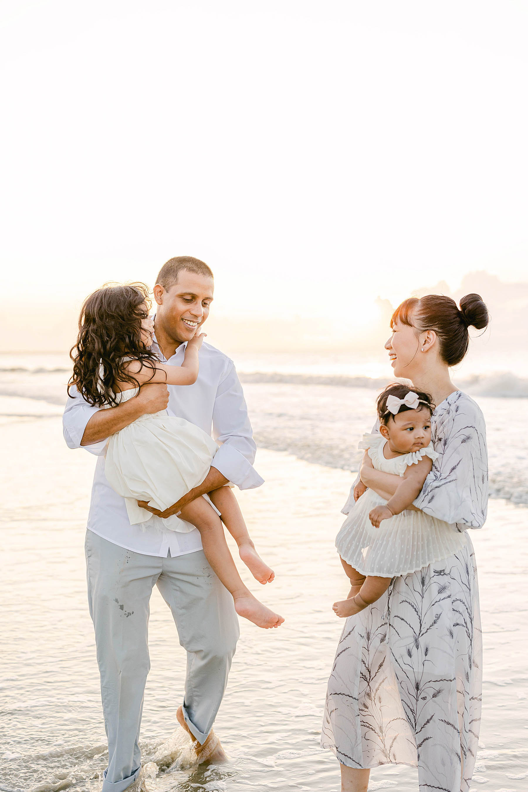 family standing together on the beach at sunrise wearing white