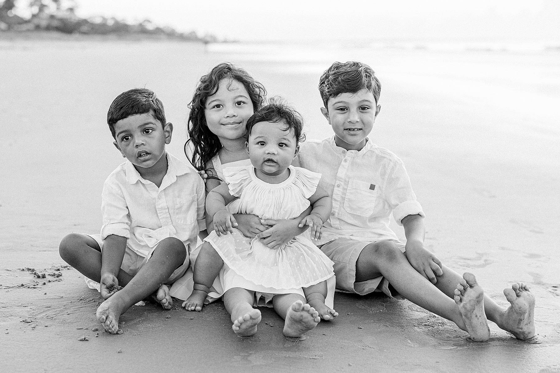 kids sitting on the beach wearing neutral colors hugging