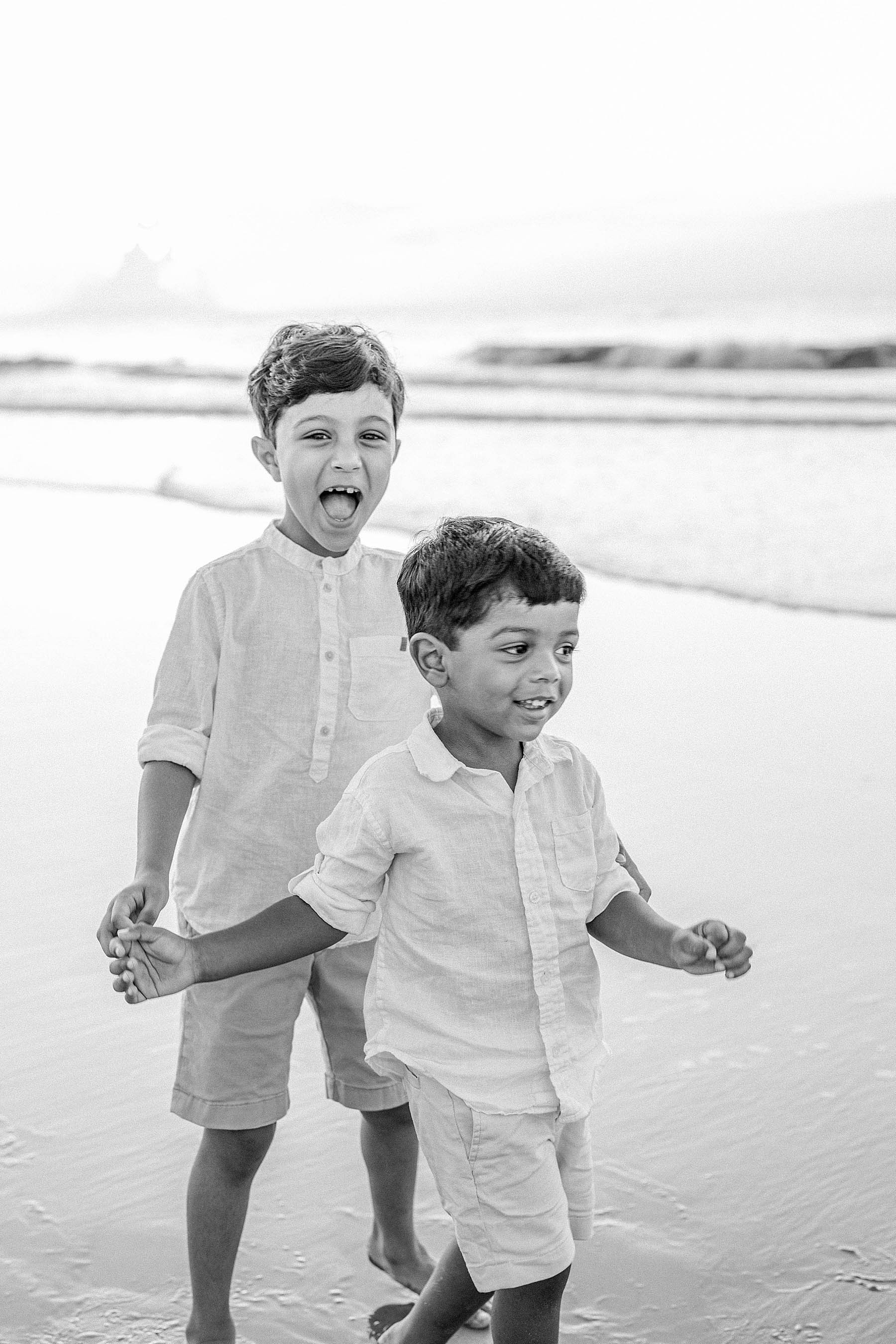 black and white image of two boys hugging each other at sunrise on the beach