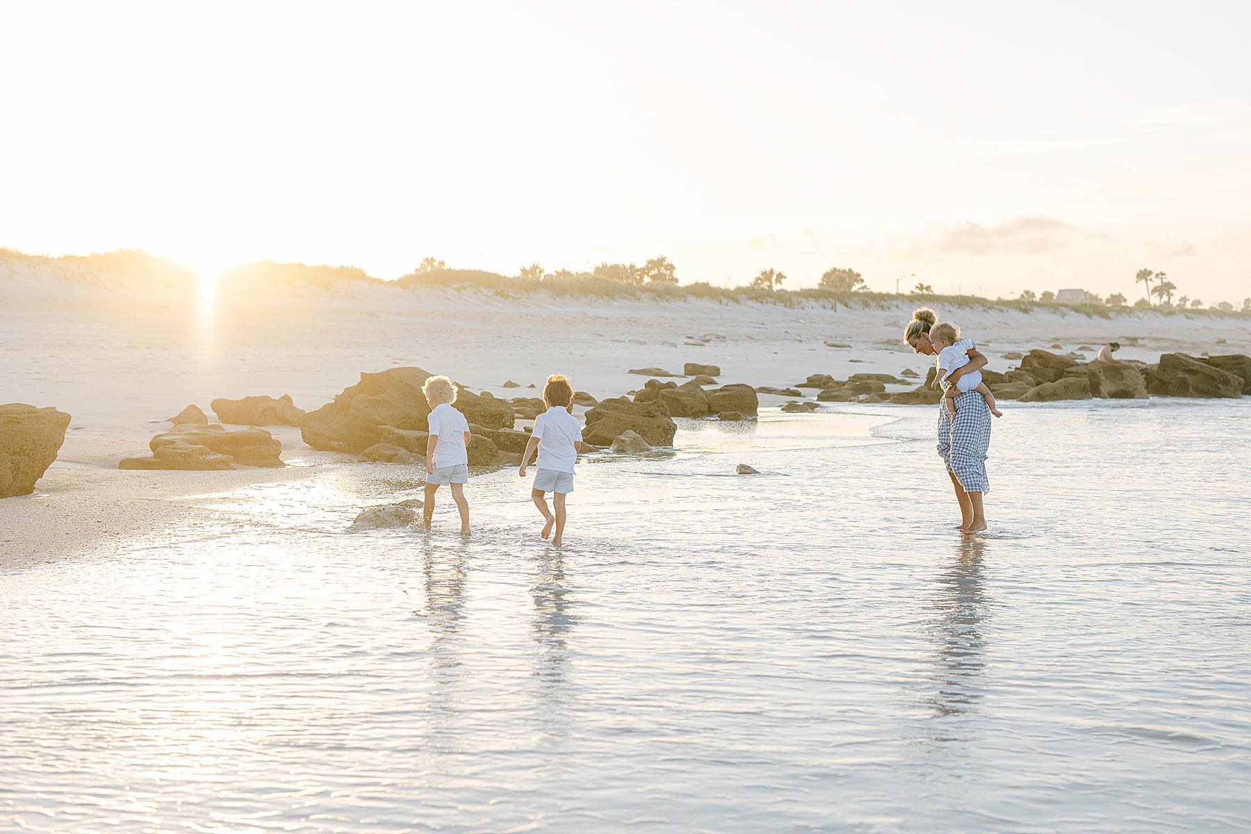 woman standing in the water on the beach with her children at sunset
