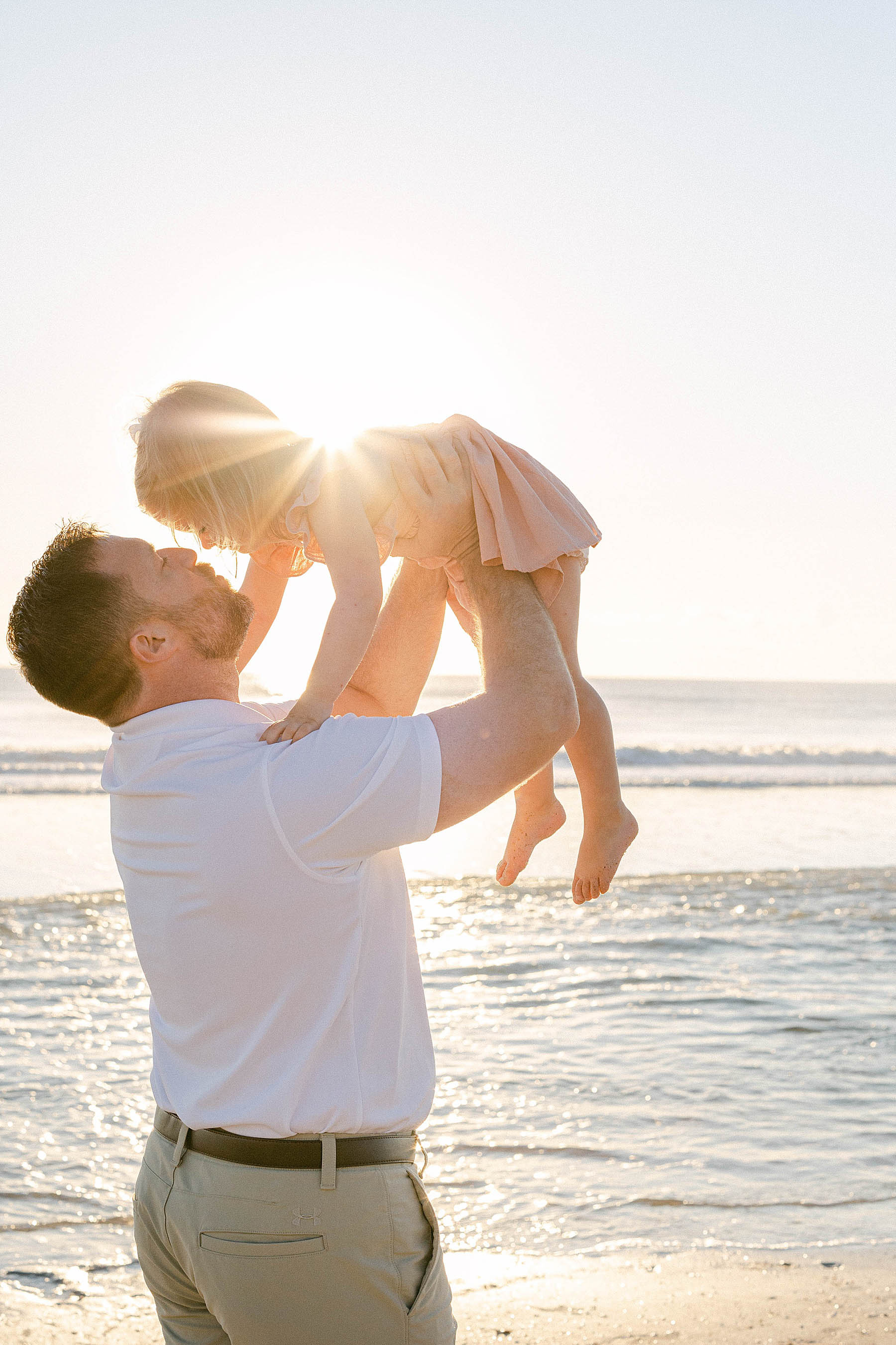 dad holding little girl backlit with sunrise shining through at the beach