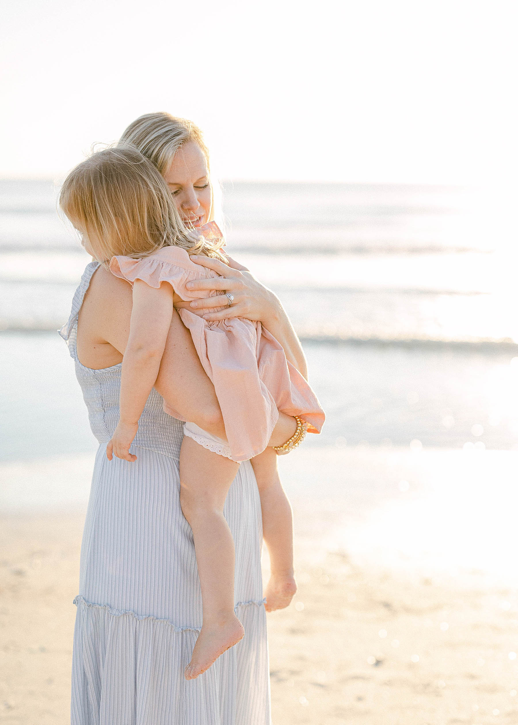 mom holding baby girl at sunrise on the beach wearing blue dress