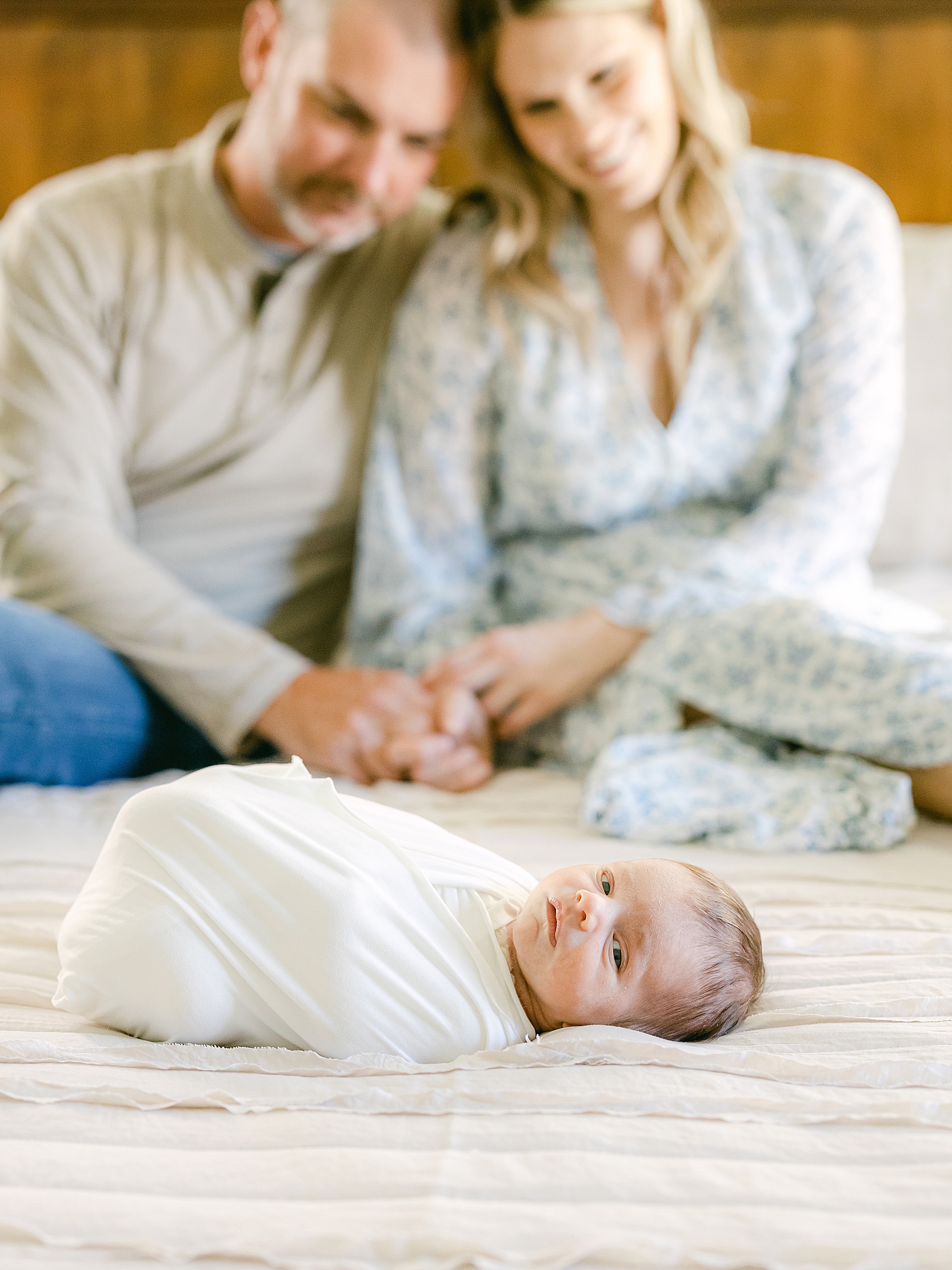 couple looking and smiling at newborn baby on the bed