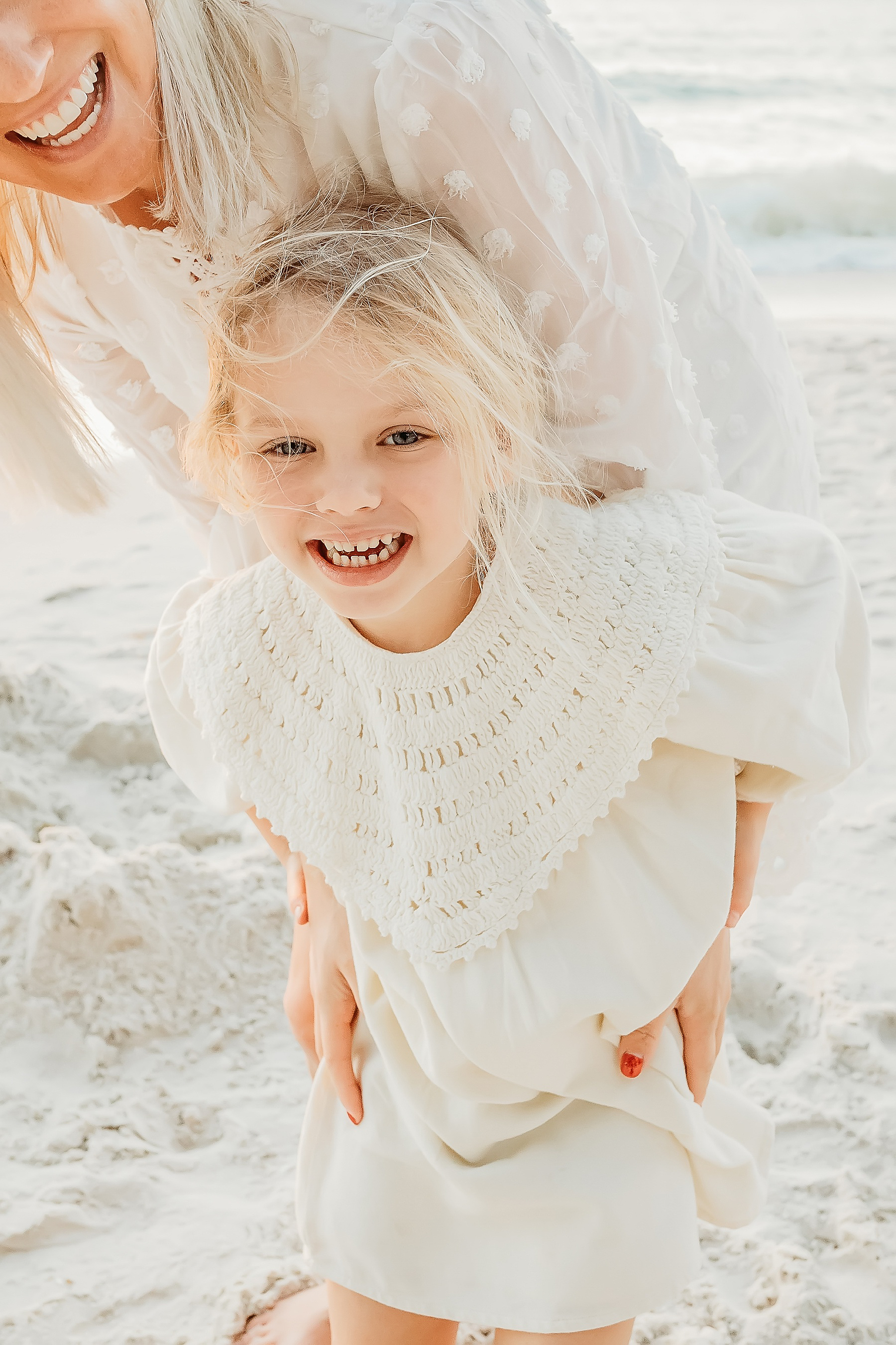woman in white dress chasing little blonde girl in white dress smiling on the beach Naples Florida