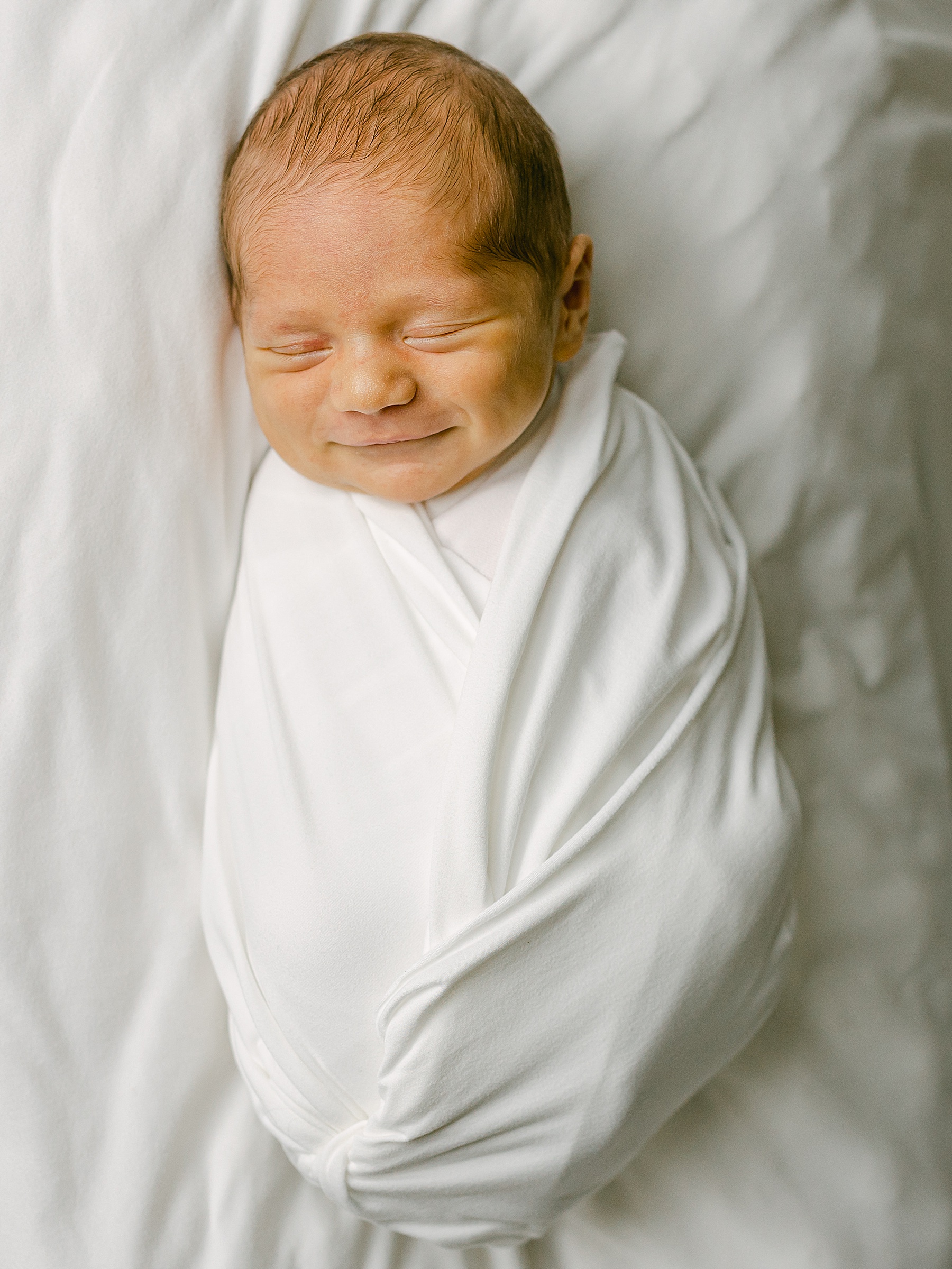 newborn baby boy smiling wrapped in a white blanket