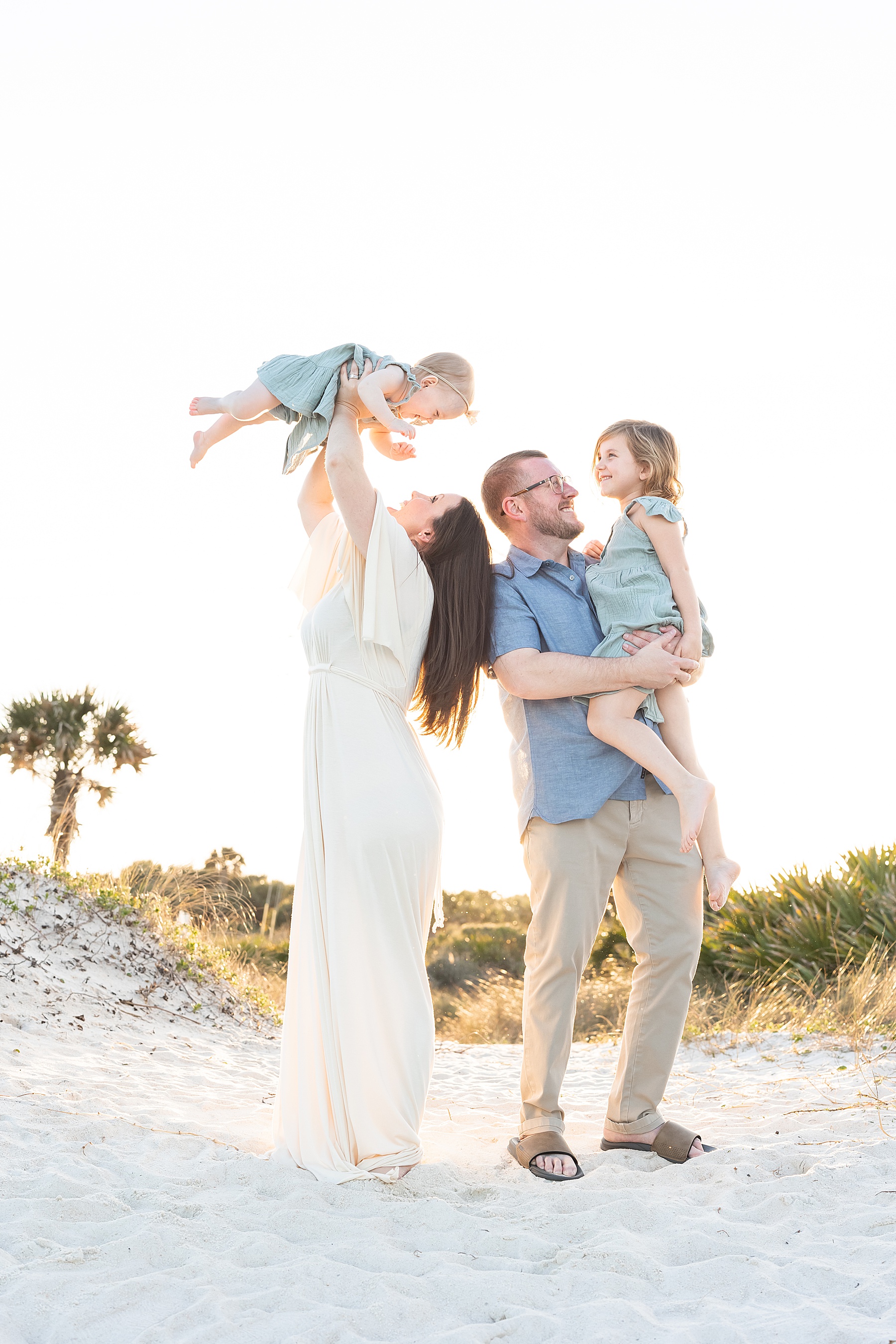 family throwing little baby girl in the air on the beach wearing neutral colors