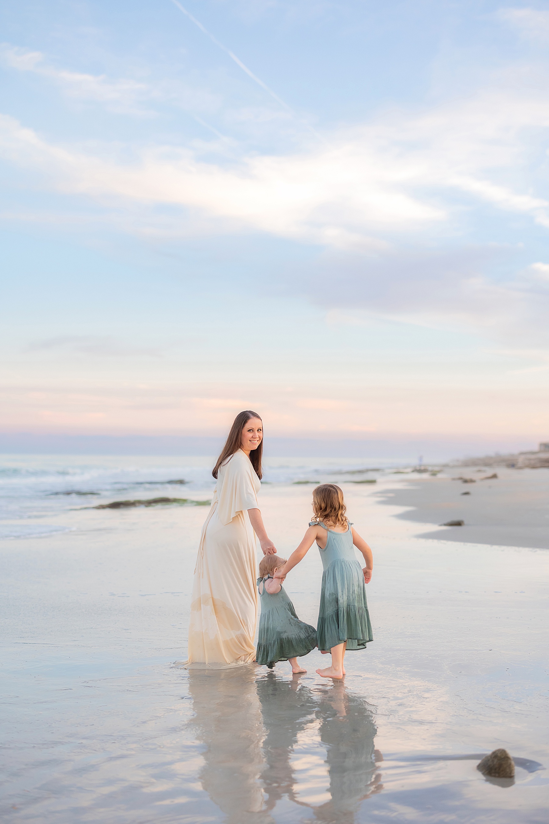 woman holding little girls hand standing on the beach with pastel sky in Florida