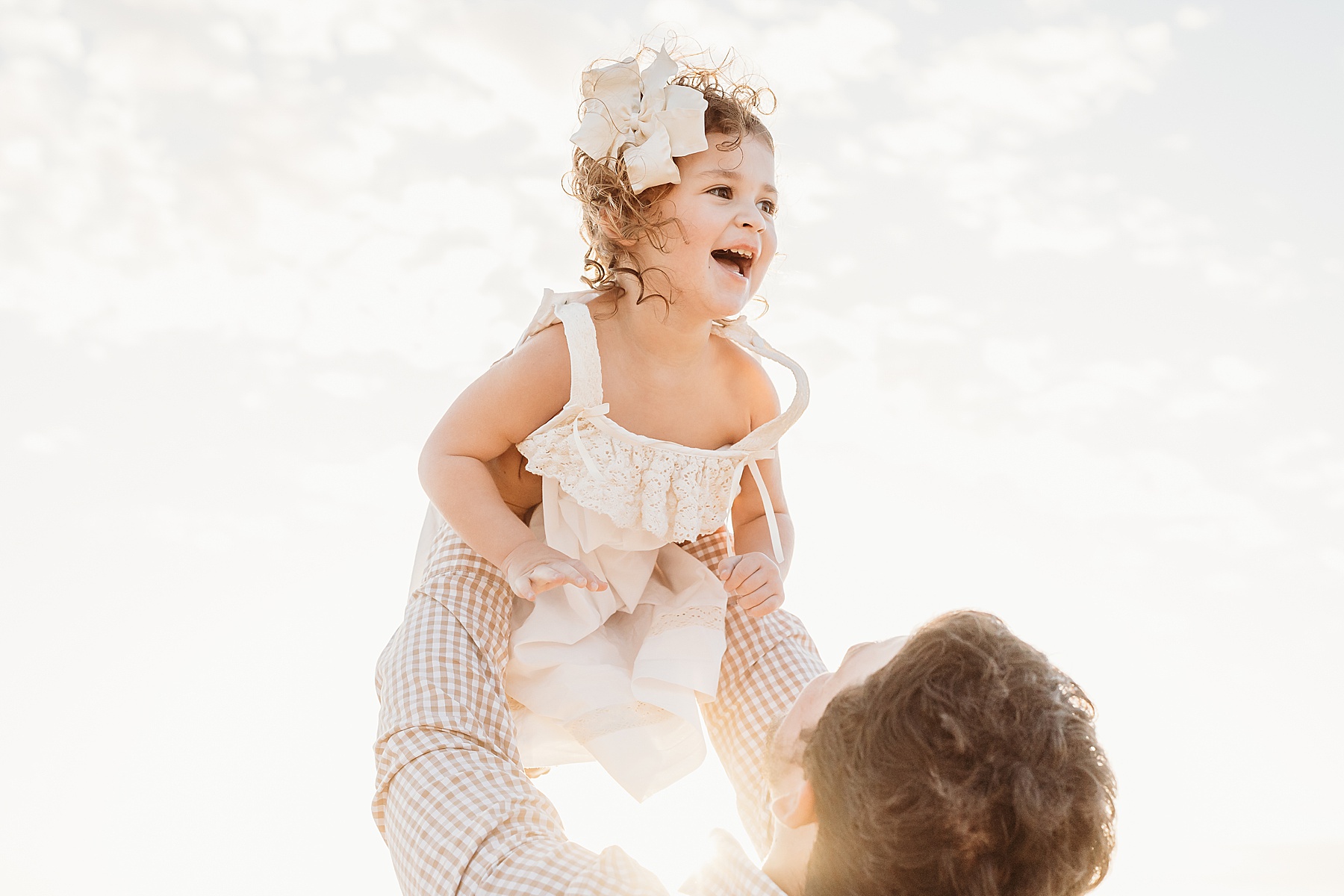man holding little girl in white dress in the air at sunrise on the beach
