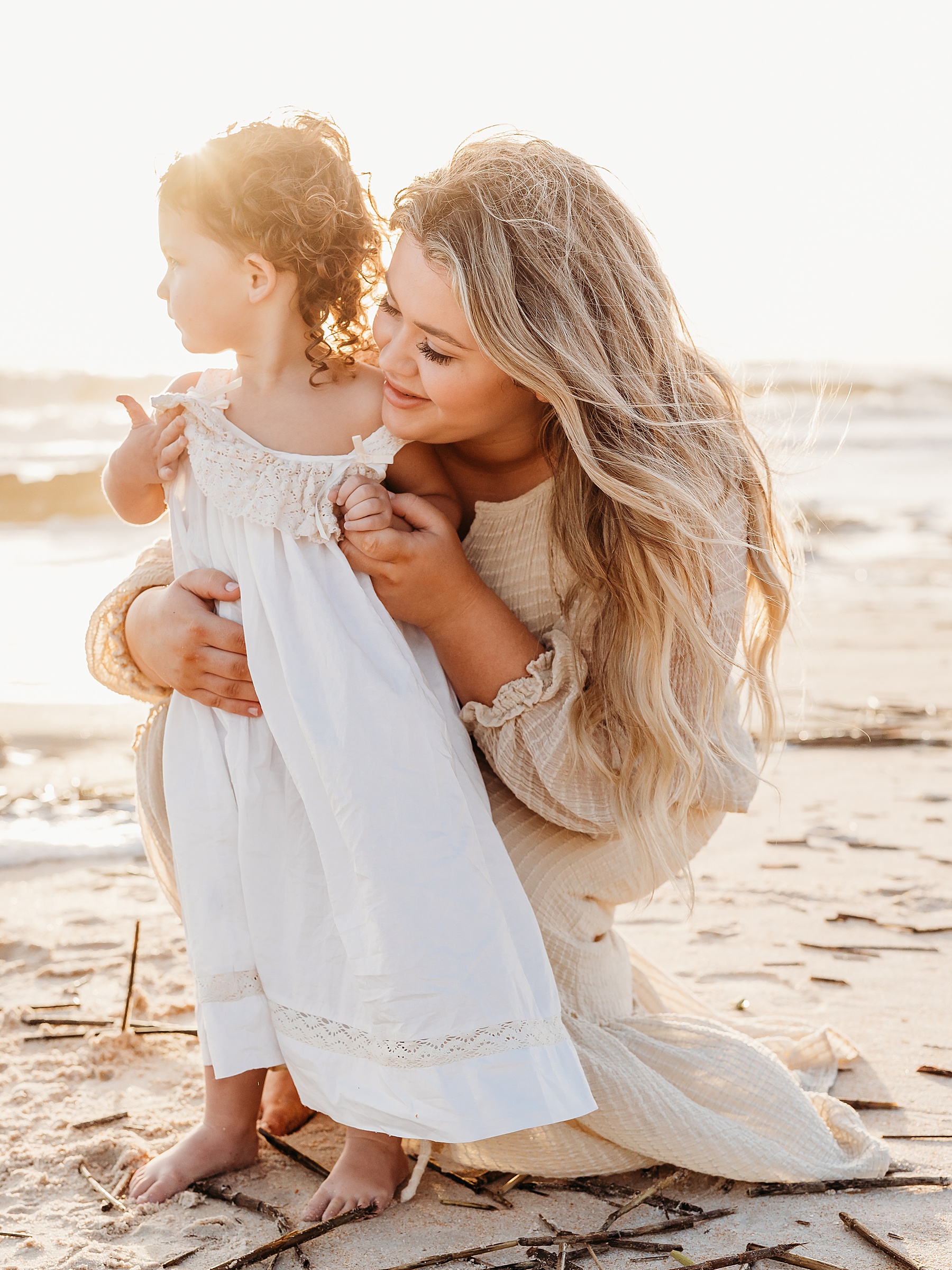 woman holding little girl in white dress on the beach at sunrise in Florida