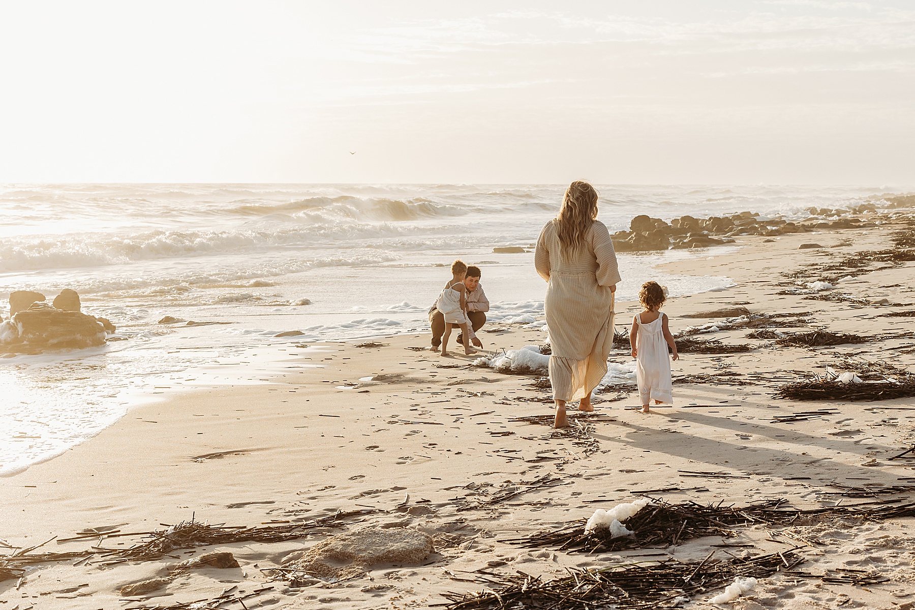 family walking on the beach at sunrise wearing neutral colors