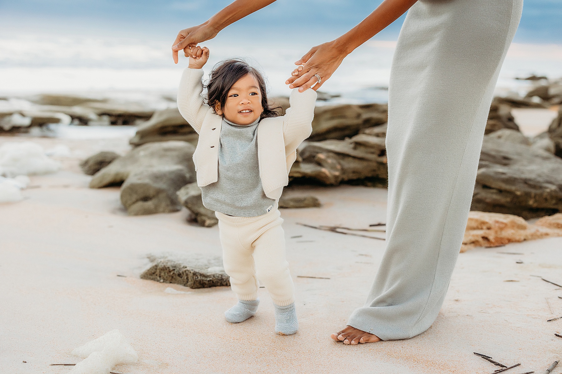 woman holding a baby boy on the beach at sunrise wearing a long neutral dress