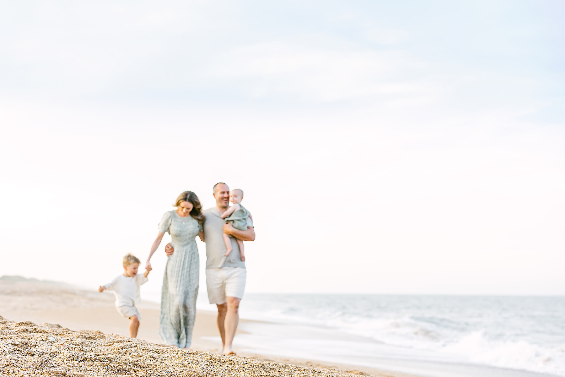 blurry photo of family walking on the beach together dressed in neutrals and sage green colors