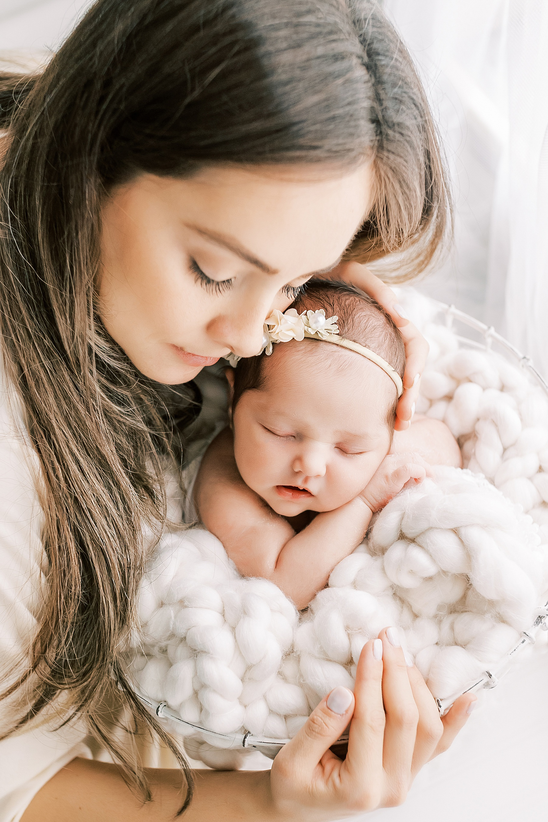 woman with long dark hair holding newborn baby in wire basket wrapped in white blanket