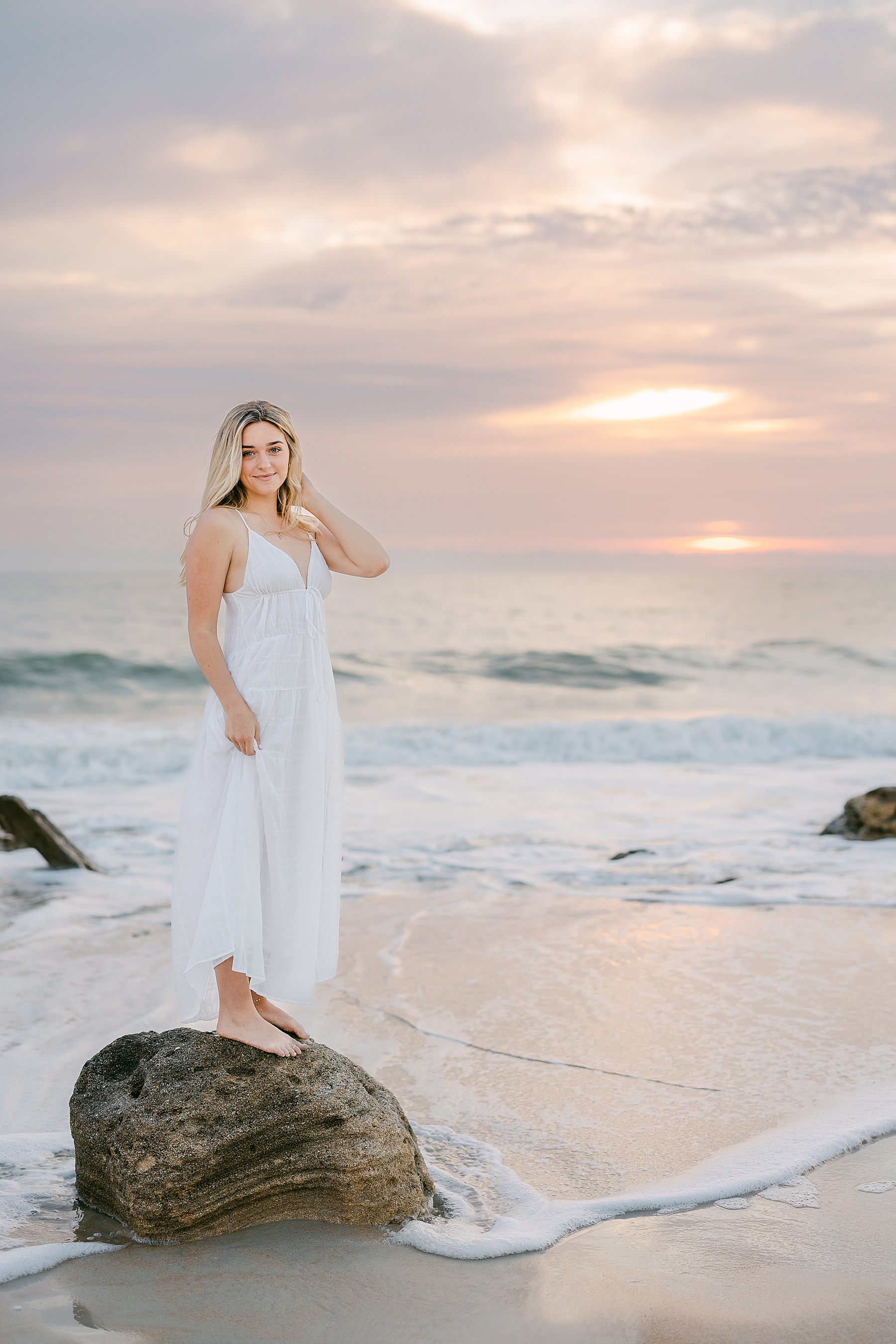 blond woman standing on the rocks at a pastel sunrise on the beach in st. augustine florida