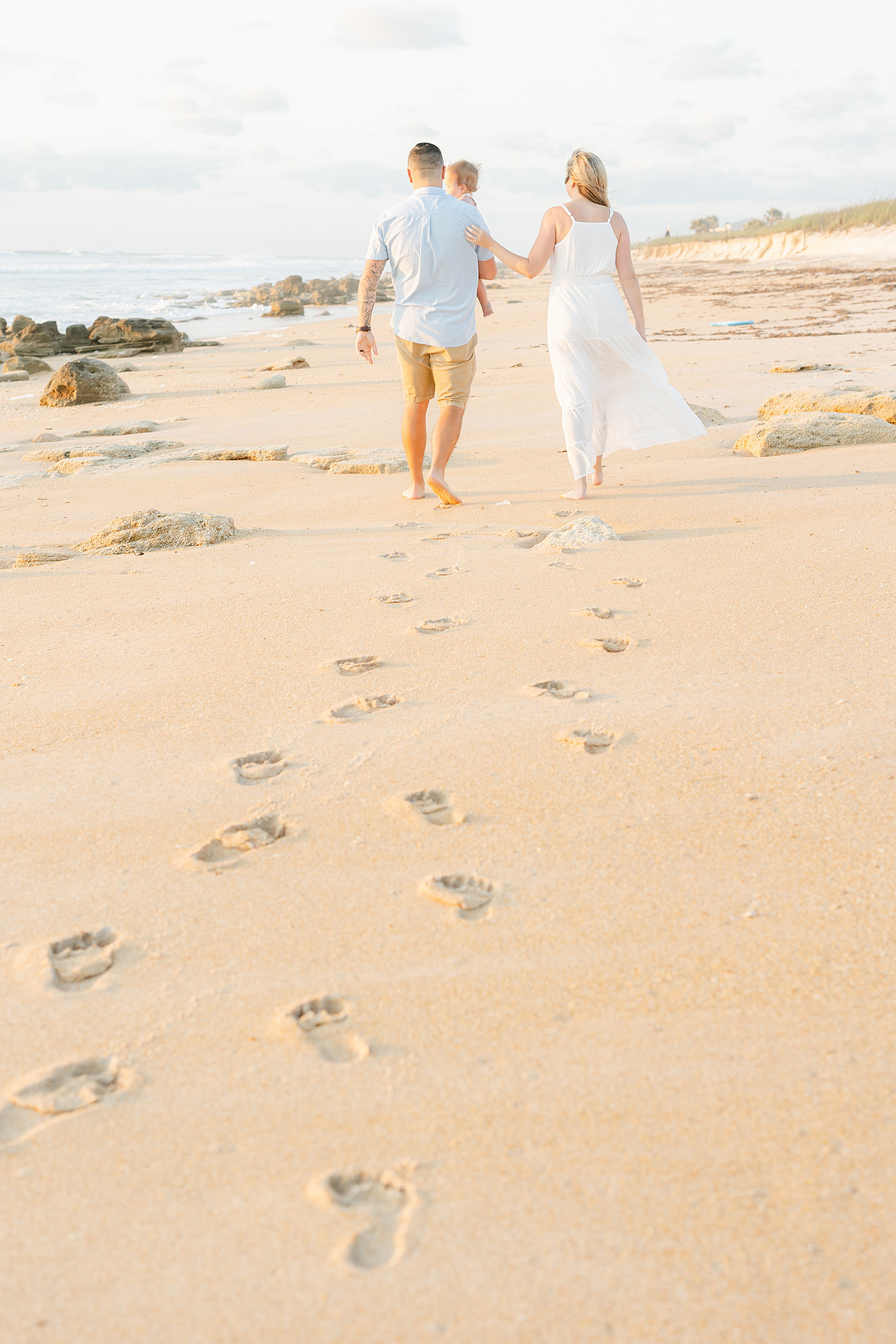 man and woman walking in the sand with footprints on the beach at sunrise